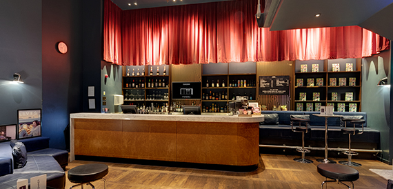 Bar counter beneath a red curtain with shelves of bottles