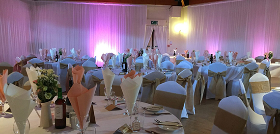 Banqueting tables dressed in white linen with purple lighting and floral displays.