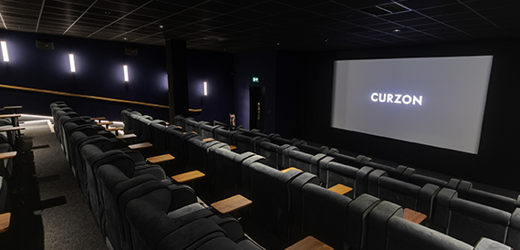 Cinema screening room with grey seats facing an illuminated Curzon screen