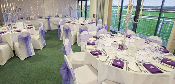 Wedding reception set with purple sashes and candelabra overlooking the racecourse