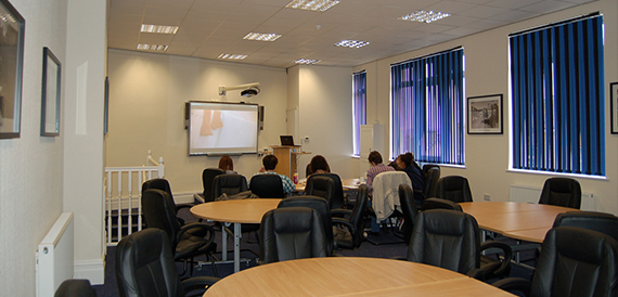 Training room with round tables, black chairs and a wall-mounted screen