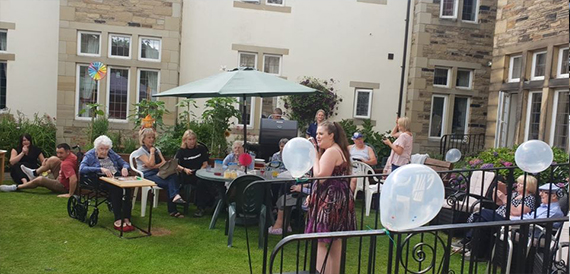Garden gathering with people seated at tables under a parasol
