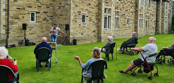 Outdoor audience seated on a lawn watching a presenter