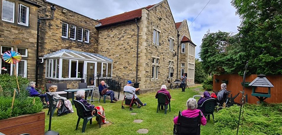 Stone building with a conservatory extension and people seated on the lawn