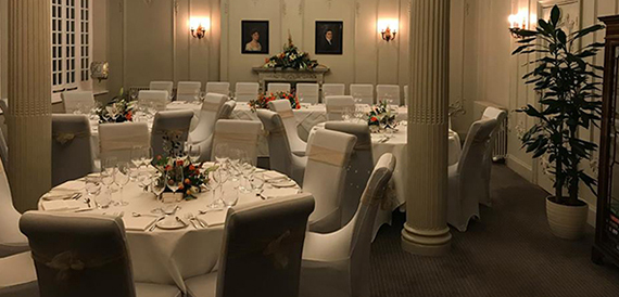 Formal dining room with white chair covers set beneath ornate columns