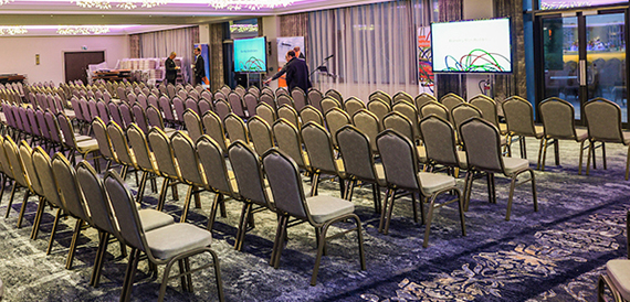 Conference room set theatre-style with rows of chairs facing presentation screens