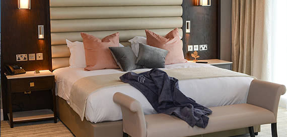Hotel bedroom with a bed dressed in pink and grey cushions