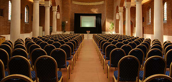 Auditorium with rows of blue and gold chairs facing a stage screen.