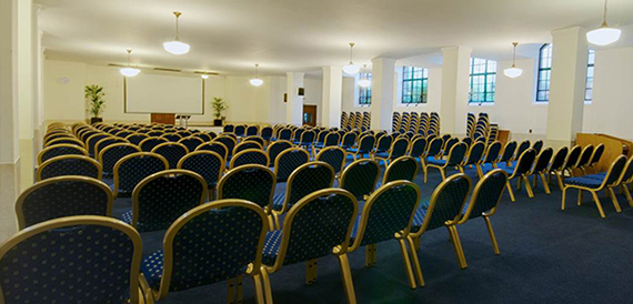 Conference room set theatre-style with rows of gold-trimmed chairs and large windows.