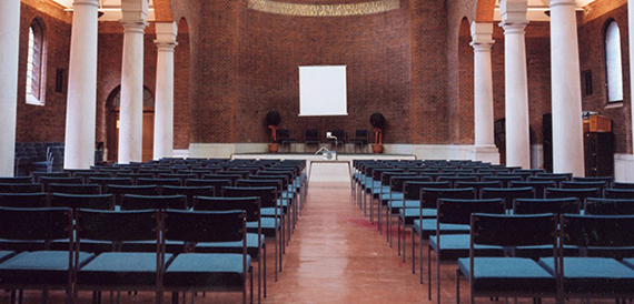 Domed auditorium with rows of blue tip-up chairs facing a large projector screen.
