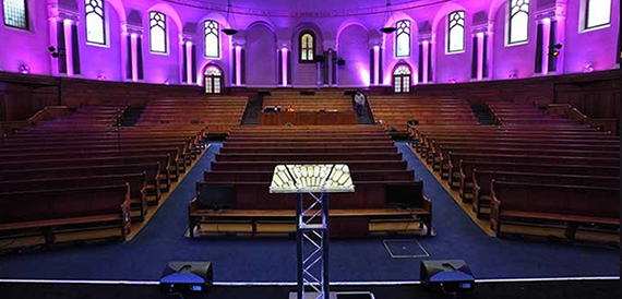 Church-style auditorium with wooden pews and a lectern lit in purple.