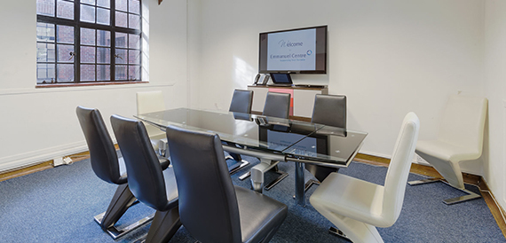 Boardroom with a glass table, black leather chairs and a wall-mounted screen.