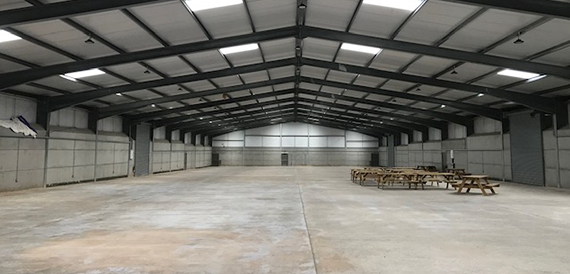 Empty steel-framed exhibition hall with a concrete floor and roof lighting.