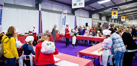 Children taking part in a cookery demonstration on a purple-draped stage.