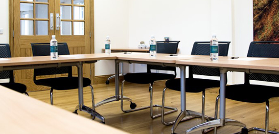 Boardroom tables arranged in a U-shape with black chairs and water bottles.