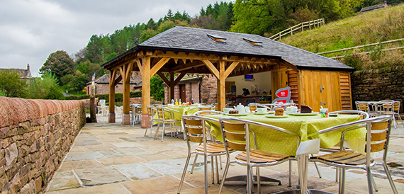 Outdoor courtyard with a wooden gazebo and tables dressed in green cloths.