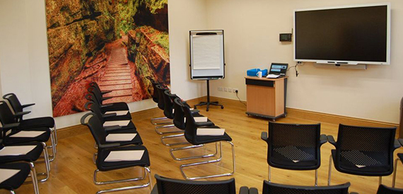 Meeting room with rows of black chairs facing a screen and flipchart.