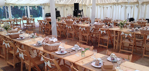 Marquee set with long wooden tables, wicker hampers and bunting for a wedding breakfast.