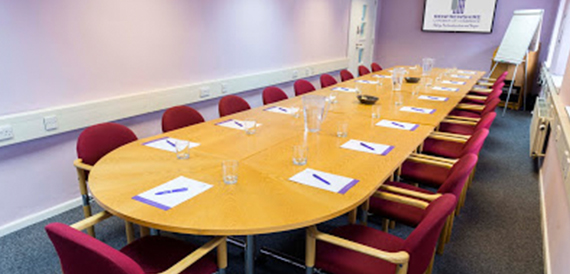 Oval wooden boardroom table with burgundy chairs and notepads laid out.