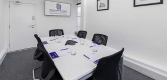 Small square boardroom table with black chairs and glasses of water.