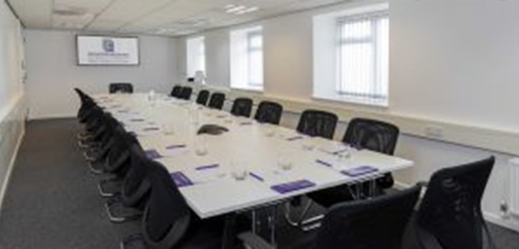 Long white boardroom table with black chairs beside curtained windows.