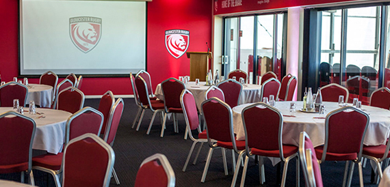 Round tables set for dining with red chairs in a branded function room.