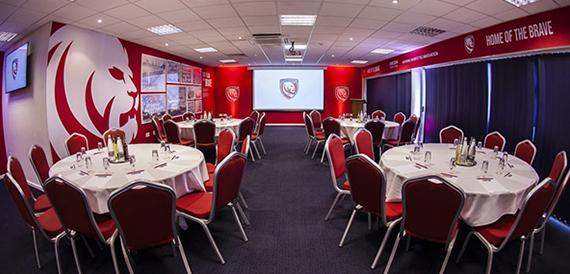 Round tables laid for dining with red chairs facing a presentation screen.
