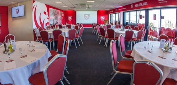 Round tables with white linen and red chairs set for a dinner event.