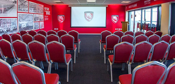 Theatre-style seating in a red-branded conference room facing a projector screen.