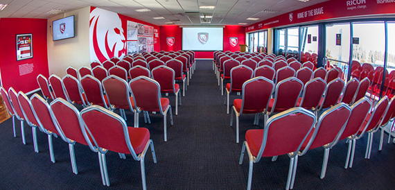 Theatre-style rows of red chairs facing a stage and screen.