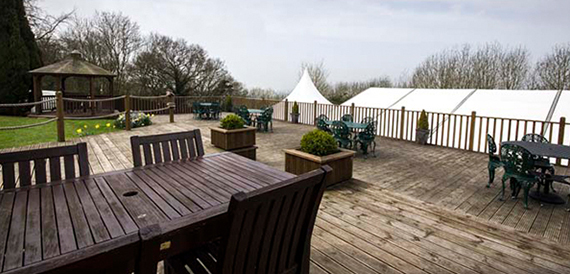 Outdoor decking with a gazebo, wooden furniture and a marquee in the background.