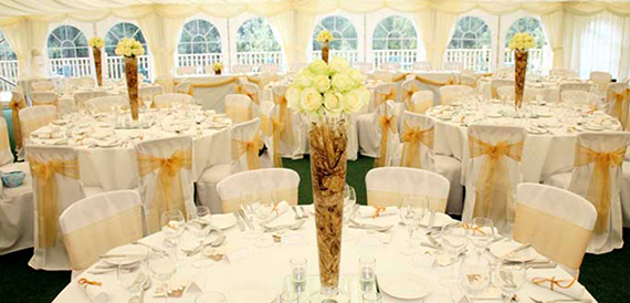 Marquee reception with round tables, gold organza sashes and tall rose centrepieces.