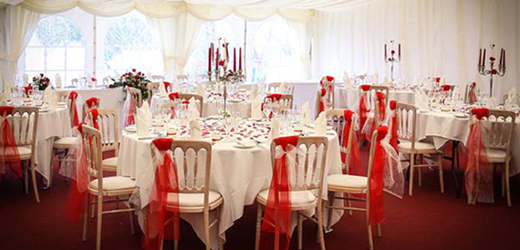 Marquee reception with round tables, red chair sashes and candelabra centrepieces.