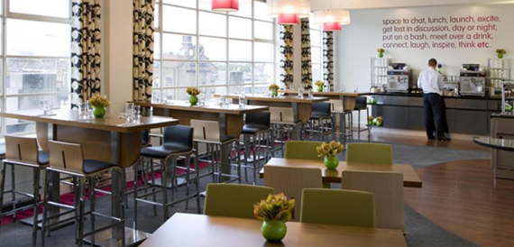 Breakout lounge with high tables, bar stools and a wall of motivational text.