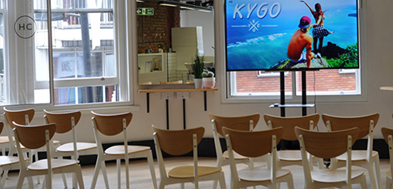 Rows of wooden chairs facing a wall-mounted screen showing event branding