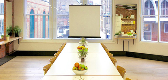 Boardroom table set with fruit bowls and water beneath a projector screen