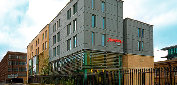 Modern hotel exterior with grey cladding and red Hampton signage.