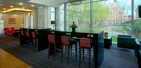 Bar lounge with striped stools along a counter and a city view through glass walls.