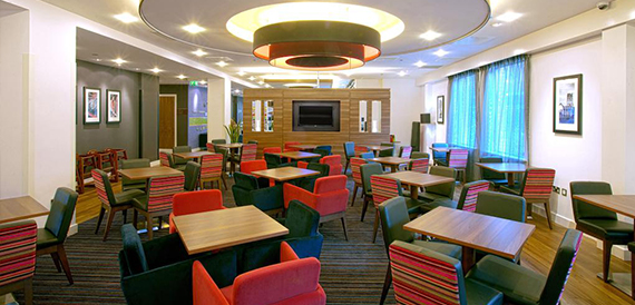 Dining lounge with round tables, colourful striped chairs and a circular pendant light.