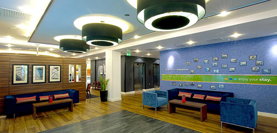 Hotel lobby with blue sofas, framed artwork and a digital welcome wall.