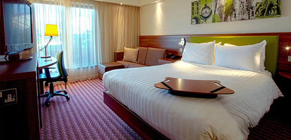 Hotel bedroom with a king bed, white linen and a small sofa area.