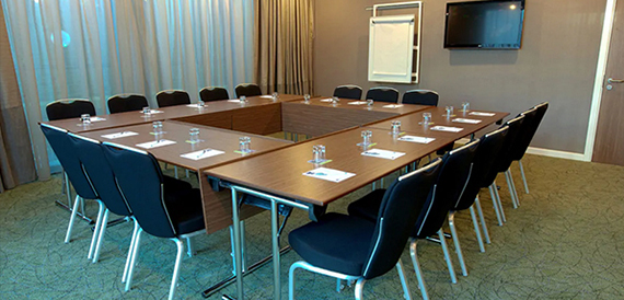 Meeting room set boardroom-style in a U-shape with black chairs and water bottles.