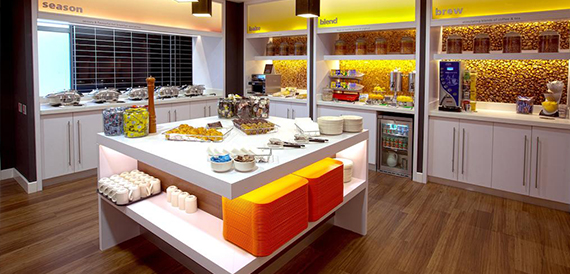 Breakfast buffet counter with labelled food stations and orange stool seating.