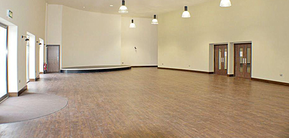 Large empty hall with a small stage, wooden floor and pendant lighting