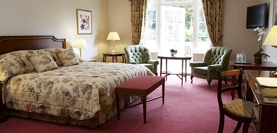 Hotel bedroom with a floral bedspread, green armchairs and a garden-facing window