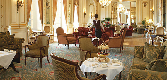 Grand drawing room set for afternoon tea with ornate chandeliers and a member of staff serving