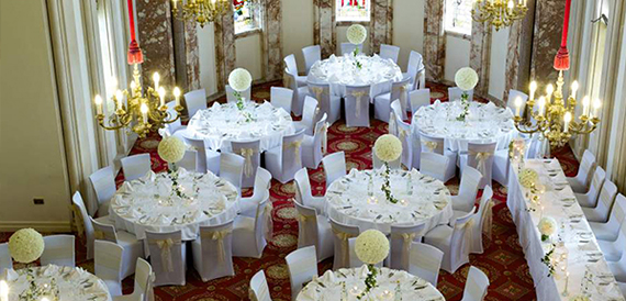 Grand hall set for a wedding banquet with round tables, chair covers and gold sashes beneath chandeliers