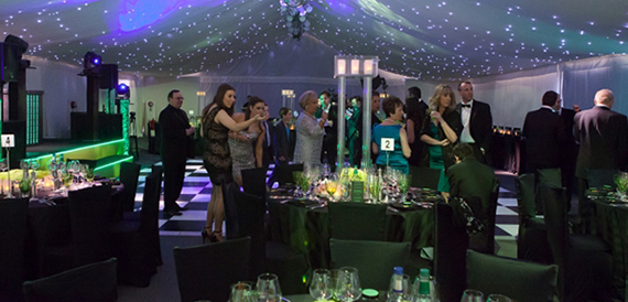 Marquee evening event with green lighting, a dance floor and guests dressed formally