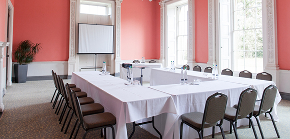 U-shaped meeting table set against coral pink walls with a projector screen