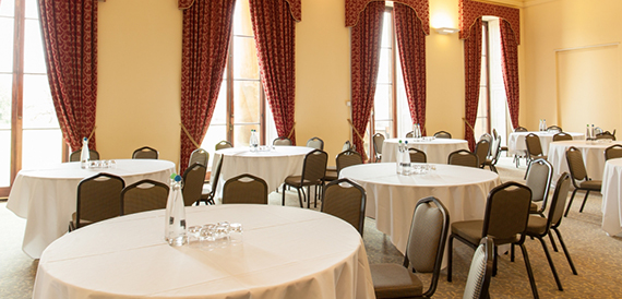 Round tables with white linen set cabaret-style beneath red curtains